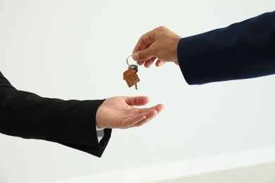 Photo of Real estate agent giving key to client on light background, closeup