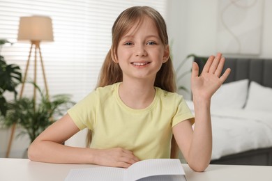 Photo of Happy little girl waving hello during online lesson indoors, view from web camera