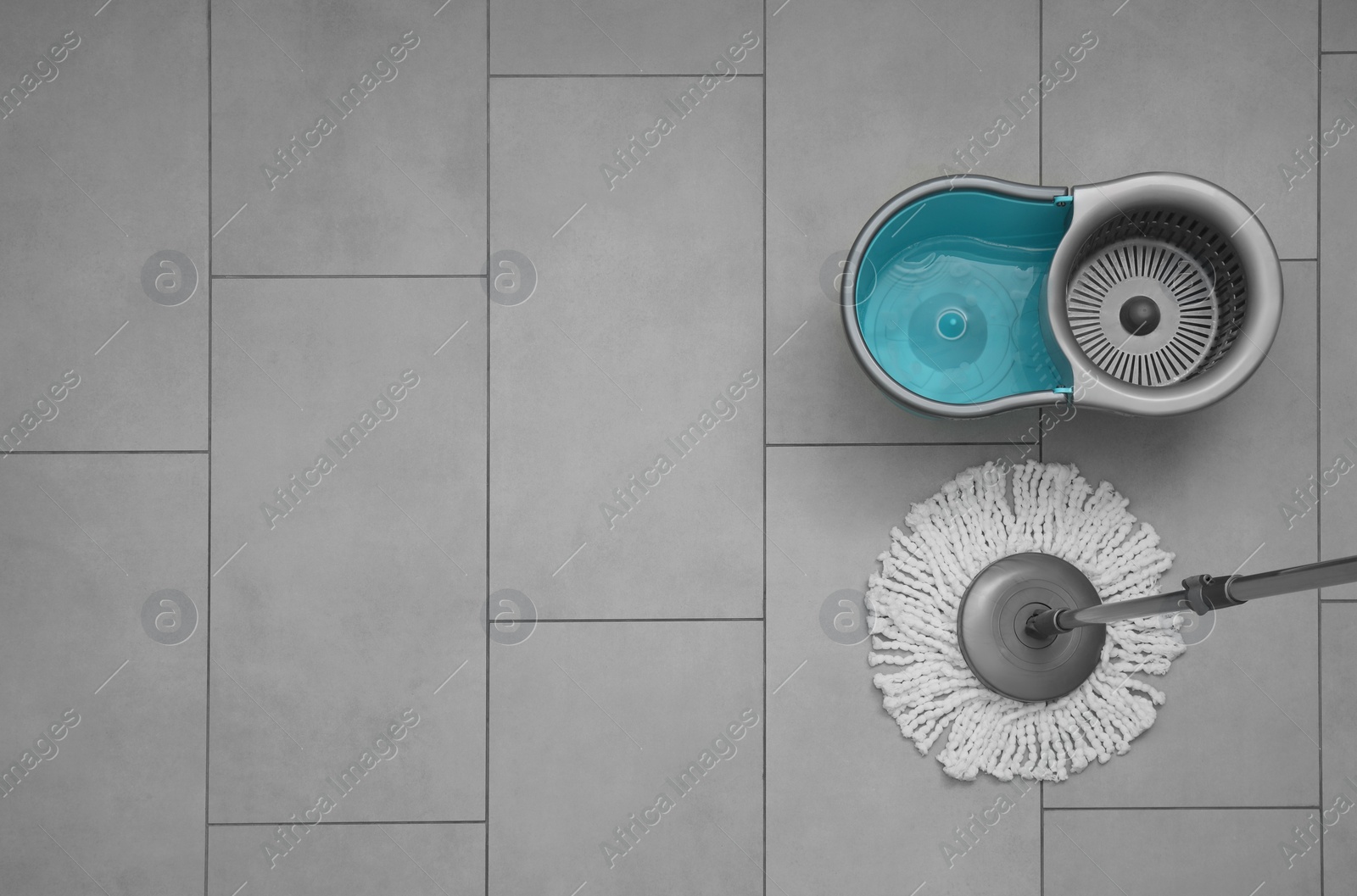 Photo of String mop and bucket on grey tiled floor, top view. Space for text