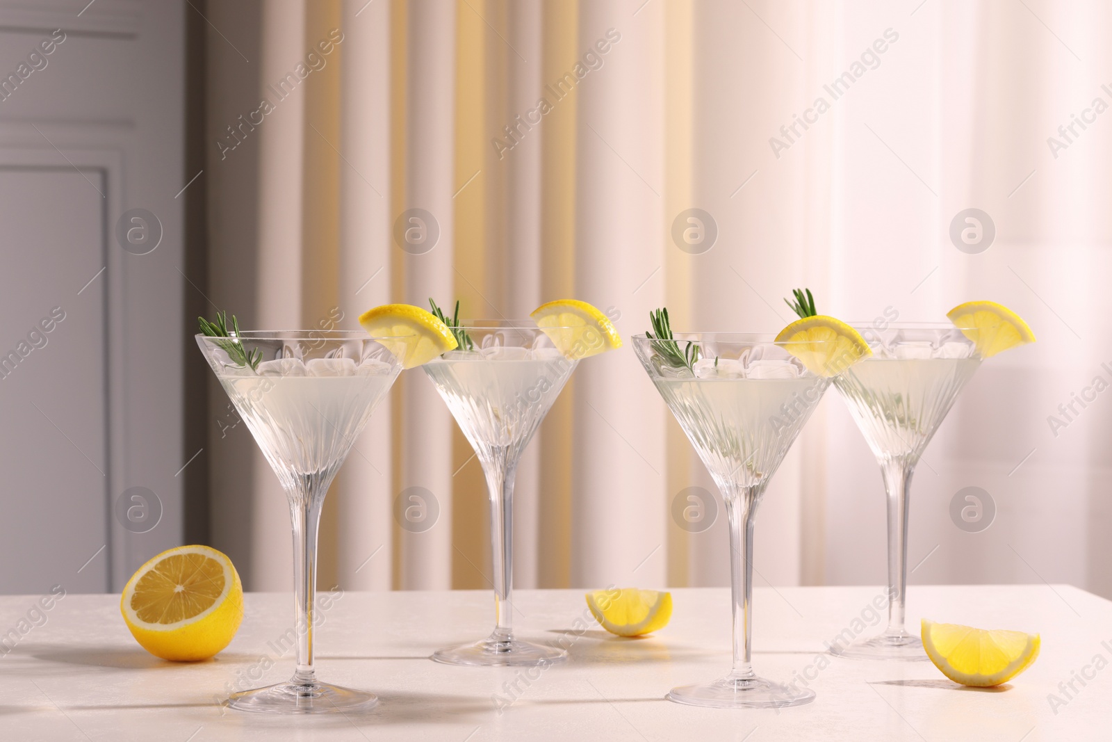 Photo of Martini glasses with fresh cocktail, rosemary and lemon on white table indoors