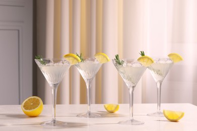 Martini glasses with fresh cocktail, rosemary and lemon on white table indoors