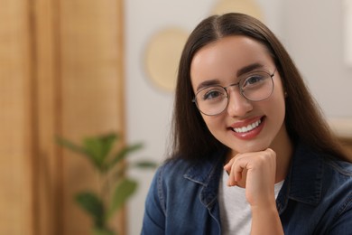 Portrait of beautiful young woman with glasses indoors, space for text. Attractive lady smiling and looking into camera