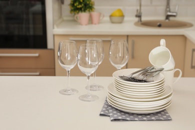 Photo of Clean dishes, glasses, cups and cutlery on table in kitchen