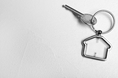 Key with trinket in shape of house on white stone background, top view and space for text. Real estate agent services