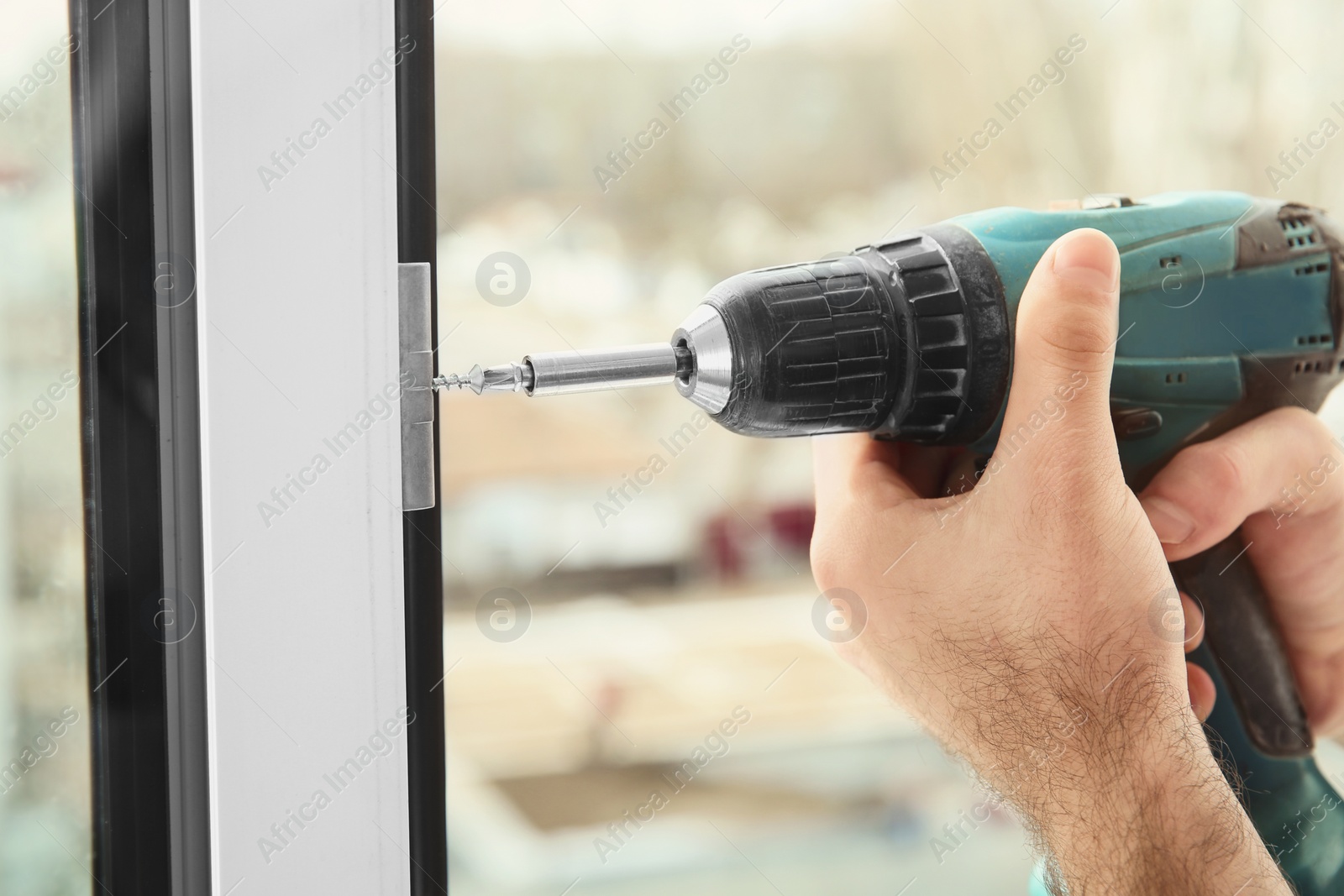 Photo of Construction worker using drill while installing window indoors, closeup