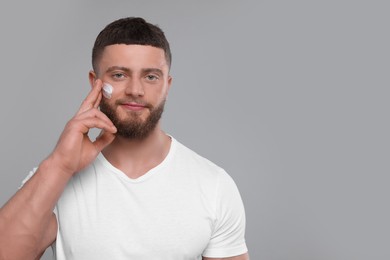 Handsome man applying cream onto his face on light grey background, space for text