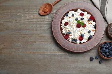 Photo of Fresh cottage cheese with berries and mint in plate on wooden table, flat lay. Space for text