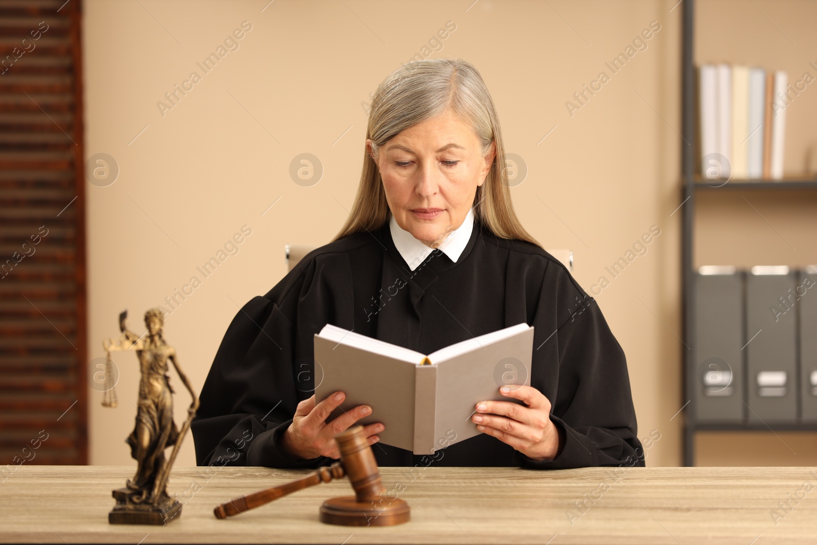 Photo of Judge reading book at wooden table indoors