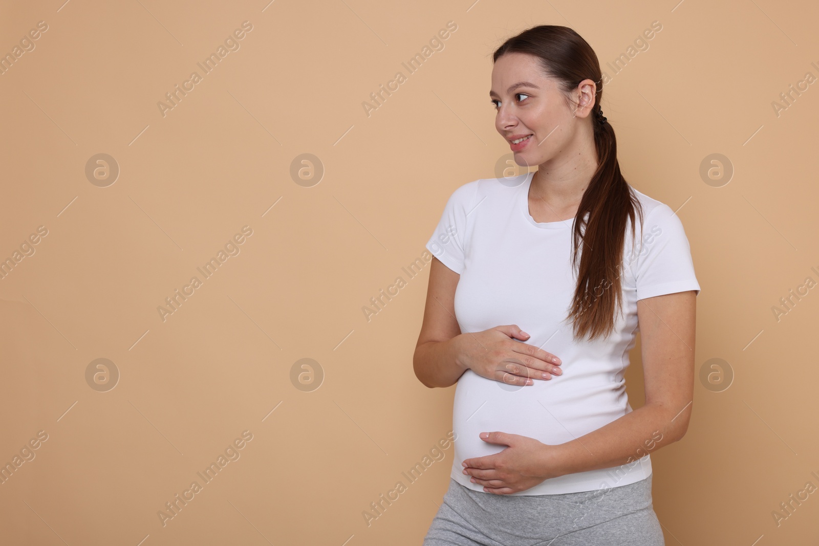 Photo of Beautiful pregnant woman in white T-shirt on beige background, space for text