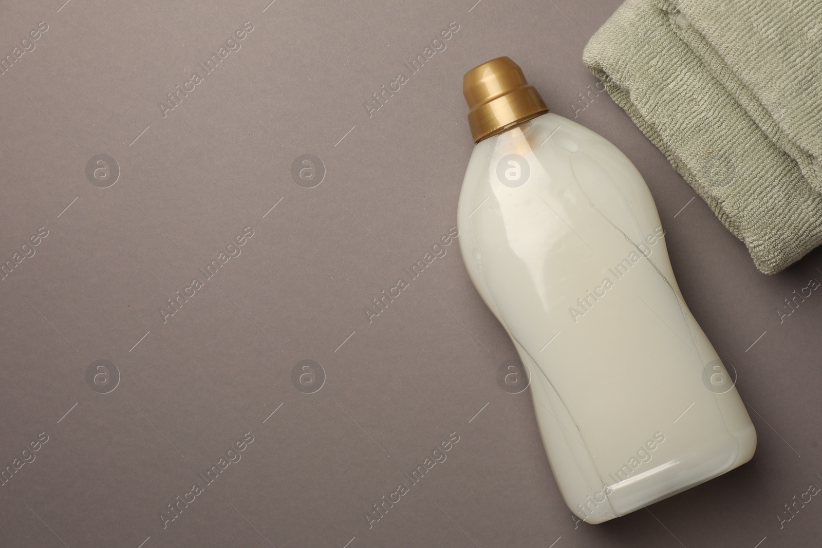Bottle of fabric softener and terry towels on gray background, flat lay. Space for text Photo of Bottle of fabric softener and terry towels on gray background, flat lay. Space for text
