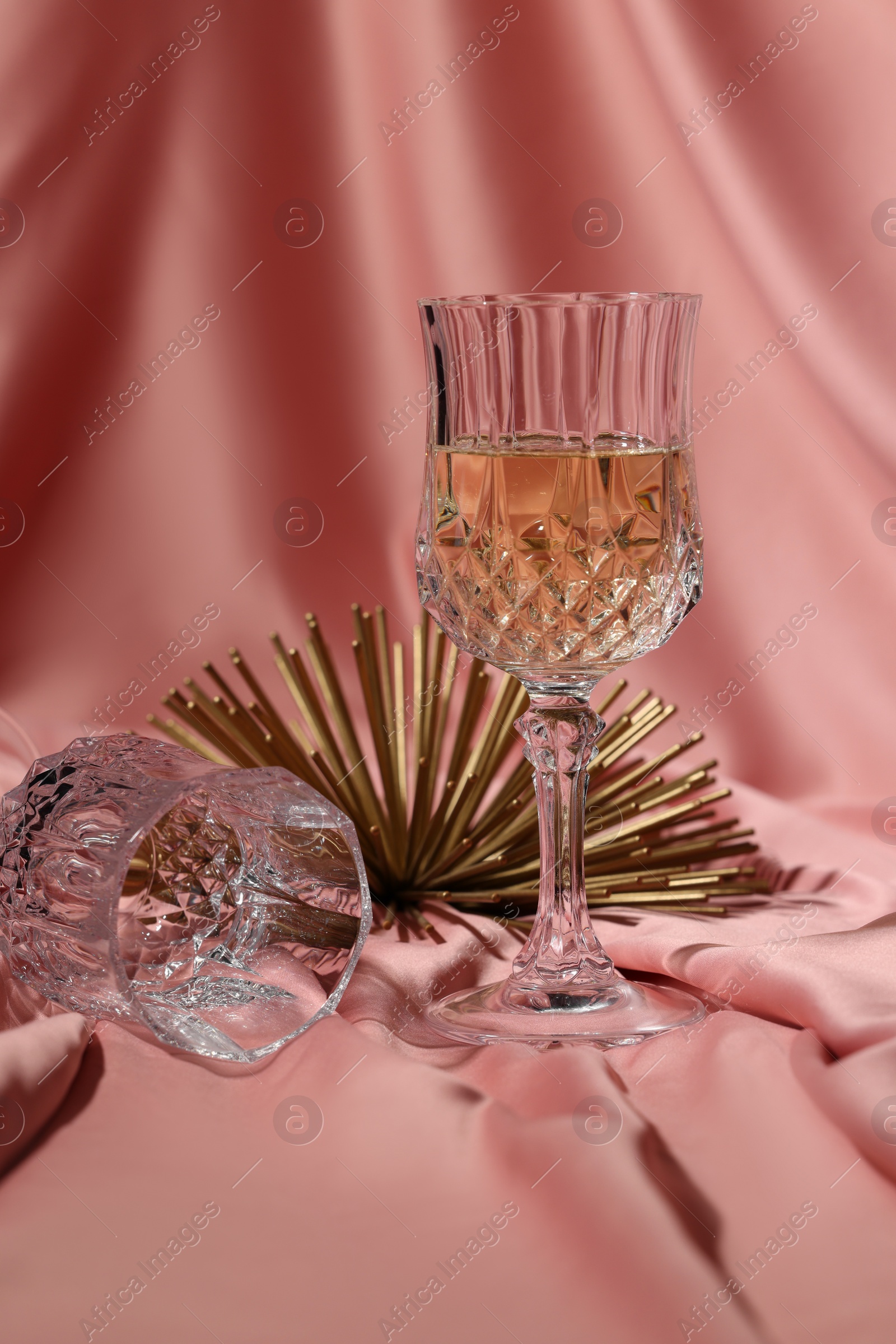 Photo of Glass of tasty alcoholic drink, empty one and golden decor on color fabric