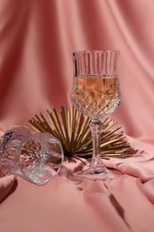 Glass of tasty alcoholic drink, empty one and golden decor on color fabric