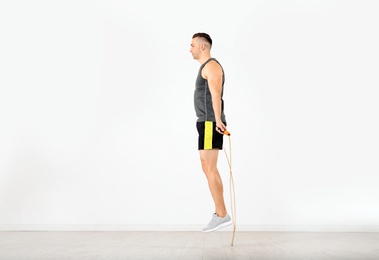 Photo of Young sportive man training with jump rope in light room