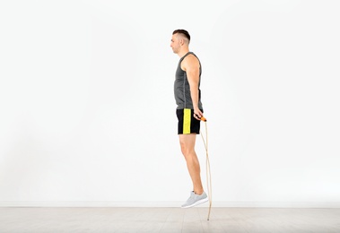 Young sportive man training with jump rope in light room