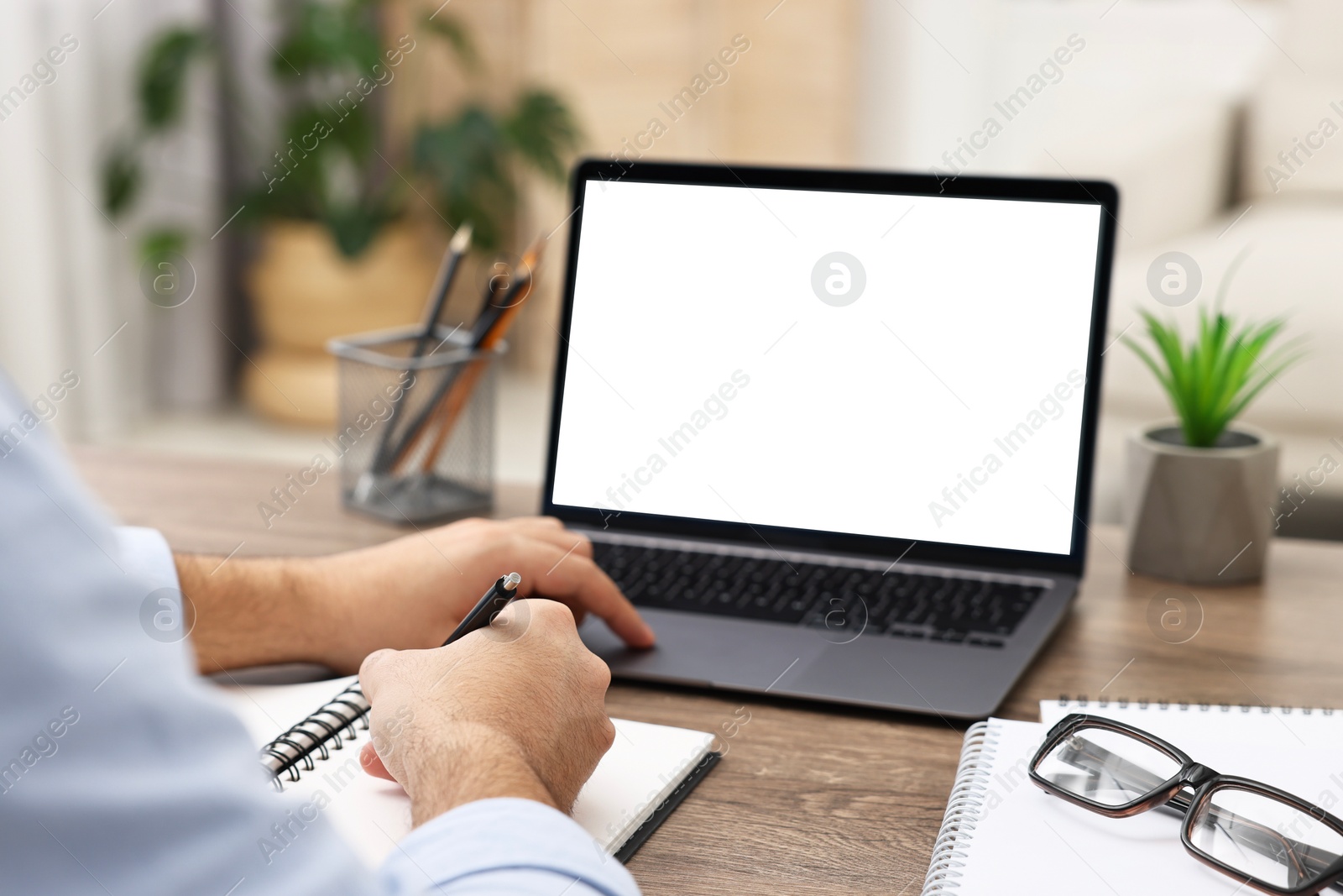 Photo of E-learning. Young man using laptop at wooden table indoors, closeup