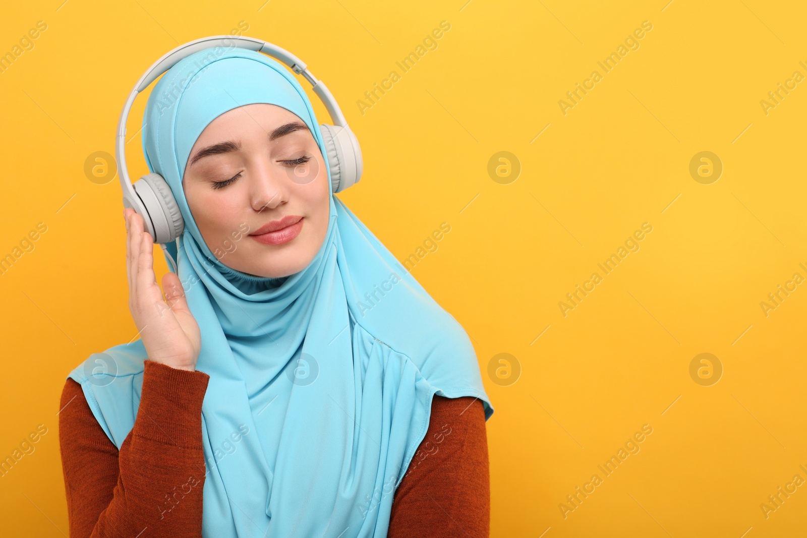 Photo of Muslim woman in hijab and headphones listening to music on orange background, space for text