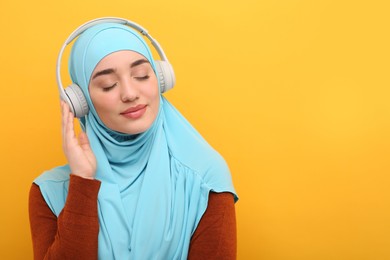 Muslim woman in hijab and headphones listening to music on orange background, space for text