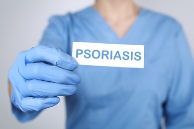 Image of Doctor holding card with word PSORIASIS on light grey background, closeup