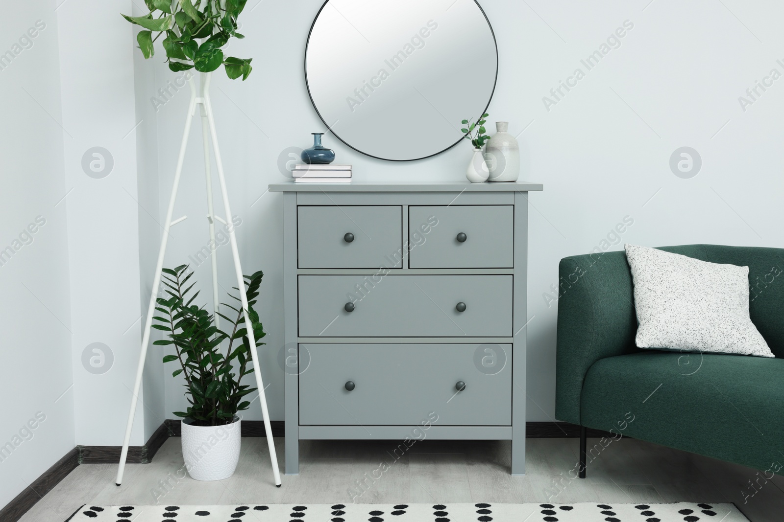 Photo of Chest of drawers and stylish round mirror on white wall indoors. Interior design