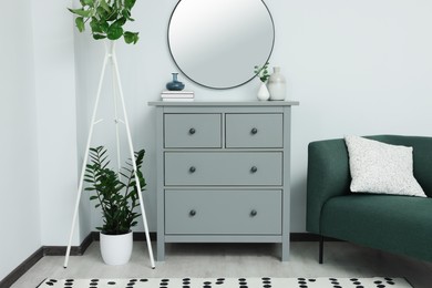 Chest of drawers and stylish round mirror on white wall indoors. Interior design