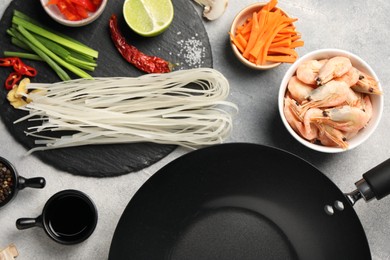 Flat lay composition with black wok, spices and products on grey textured table