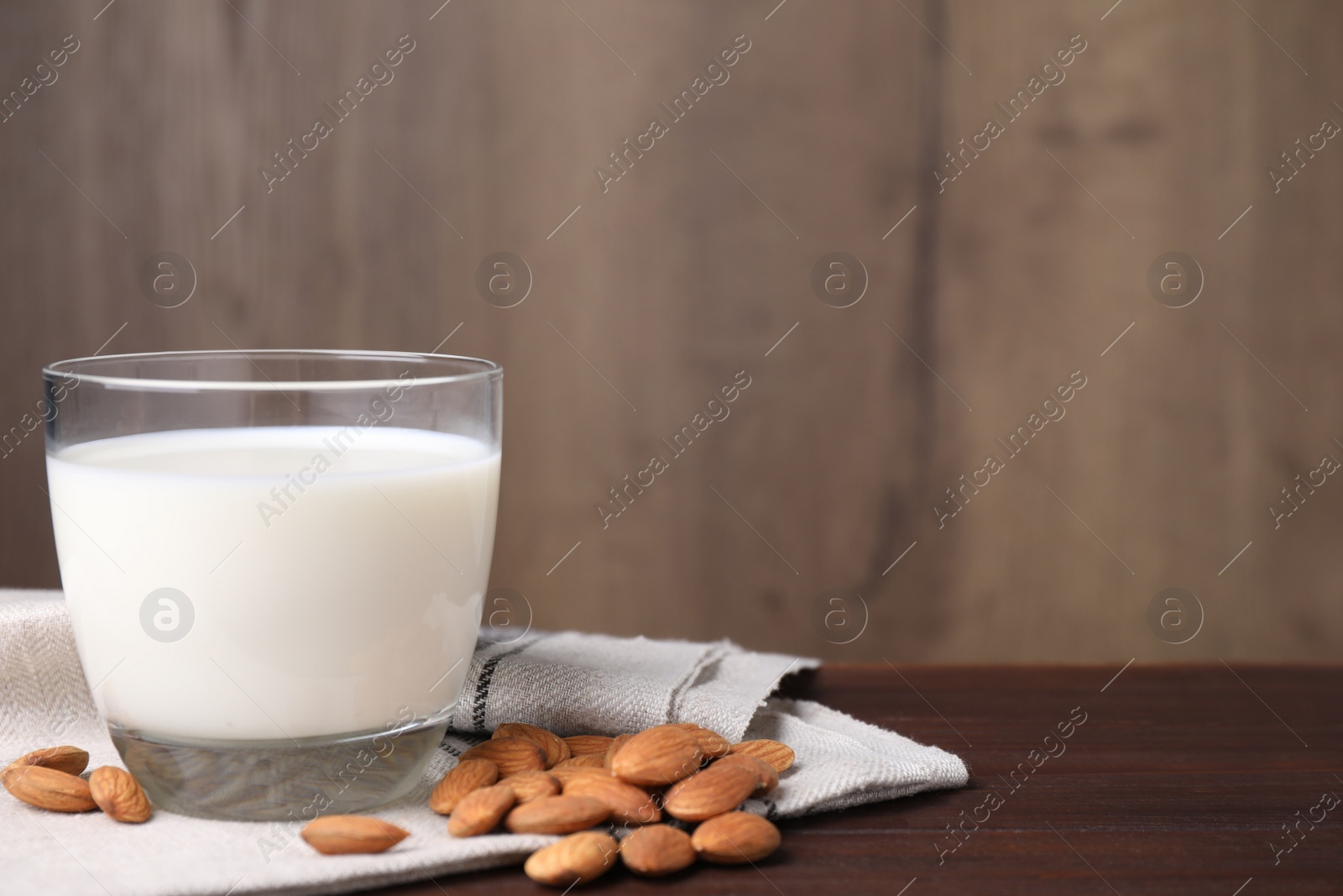 Photo of Almond milk in glass near nuts on wooden table, space for text