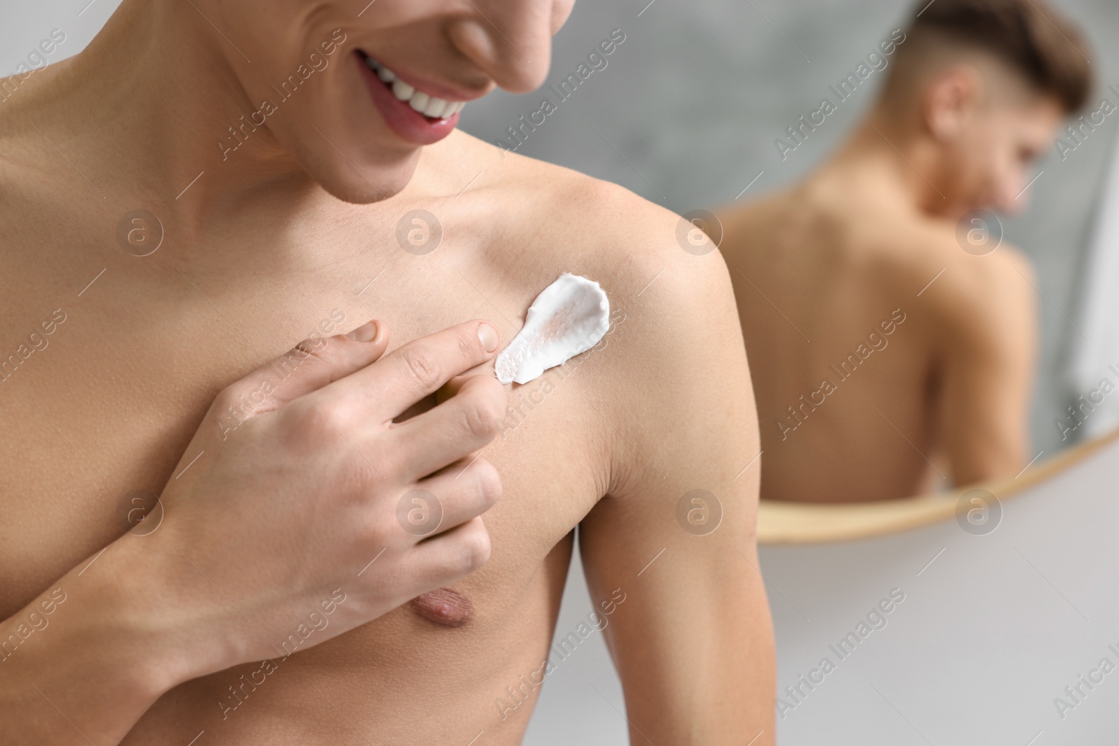 Photo of Man applying moisturizing cream onto his shoulder indoors, closeup