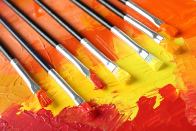 Photo of Set of different brushes on abstract colorful paint, closeup