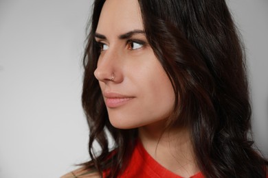 Young woman with nose piercing on grey background, closeup