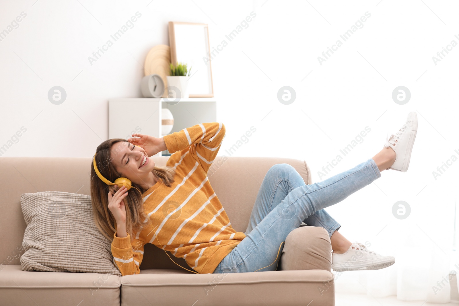 Photo of Young woman in headphones enjoying music on sofa at home