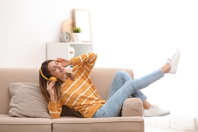 Young woman in headphones enjoying music on sofa at home