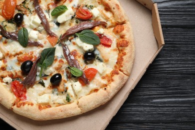 Tasty pizza with anchovies, basil and olives on black wooden table, top view
