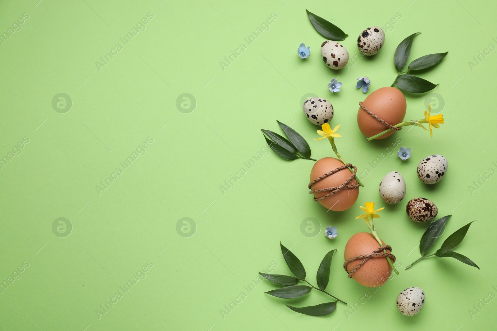 Photo of Festively decorated Easter eggs and leaves on green background, flat lay. Space for text