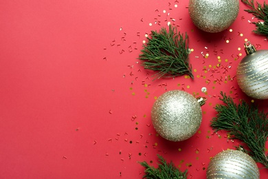 Beautiful shiny Christmas balls and fir branches on red background, flat lay. Space for text