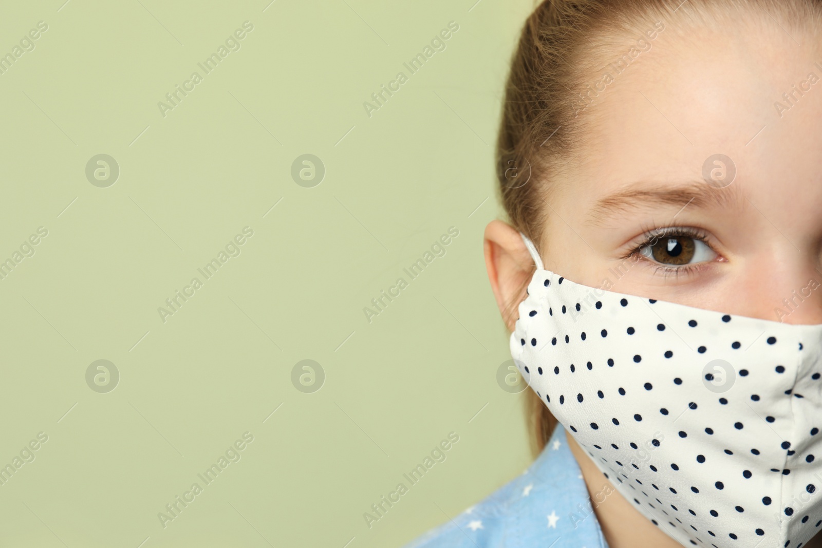 Photo of Cute little girl in protective mask on light green background, closeup. Space for text