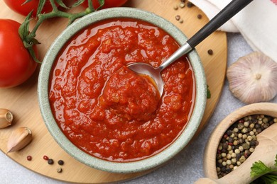 Photo of Homemade tomato sauce in bowl, spoon and fresh ingredients on light grey table, flat lay