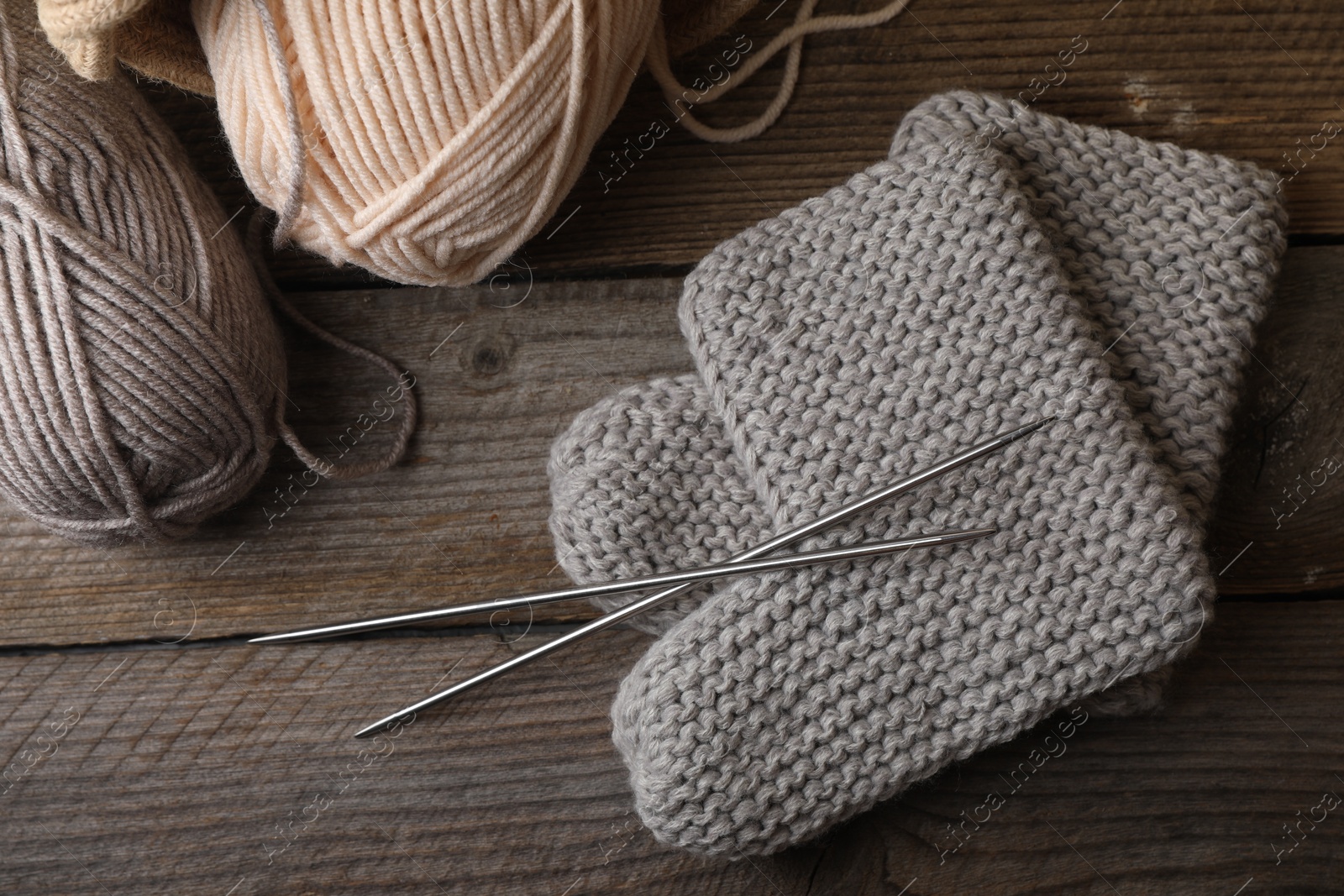 Photo of Soft colorful yarns, knitted socks and metal needles on wooden table, flat lay