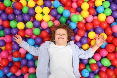 Photo of Happy little boy lying on many colorful balls, top view