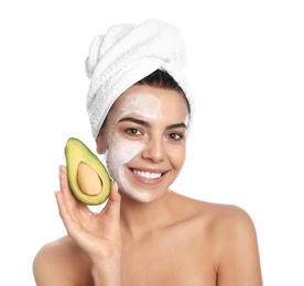 Happy young woman with organic mask on her face holding avocado against white background
