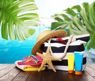 Stylish bag with beach accessories on wooden surface near outdoor swimming pool