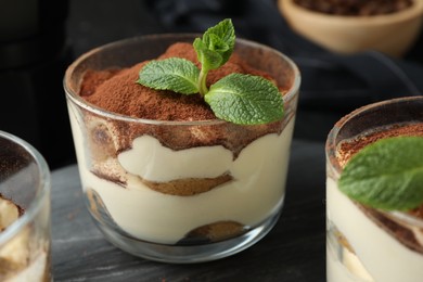 Photo of Delicious tiramisu in glasses and mint leaves on table, closeup