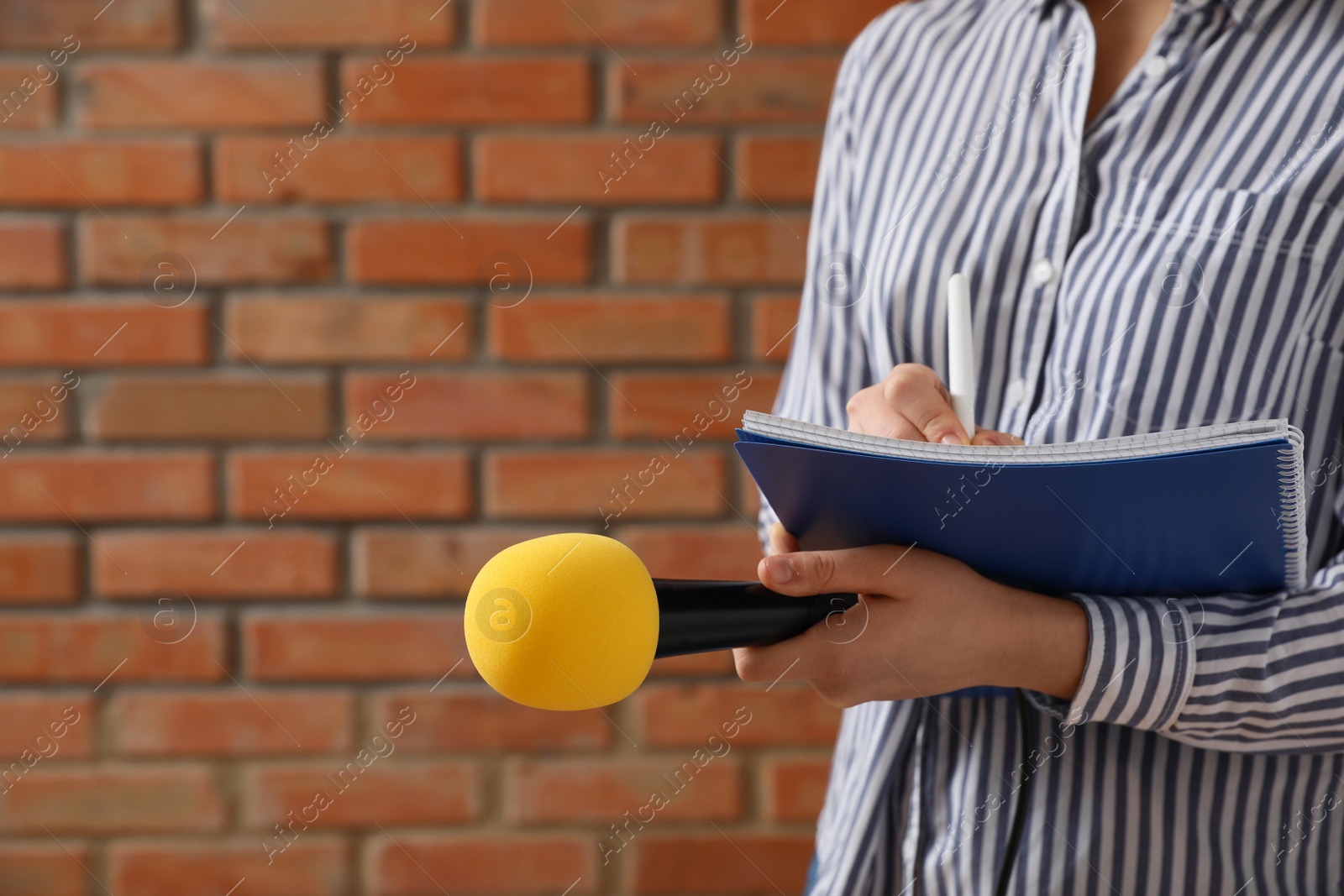 Photo of Journalist with microphone and notebook near brick wall, closeup