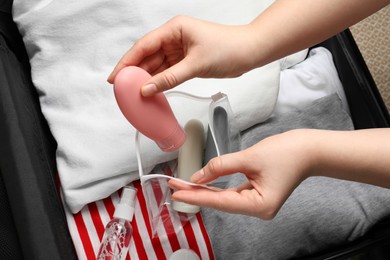 Photo of Woman putting small bottle with personal care product into plastic bag, closeup. Cosmetic travel kit