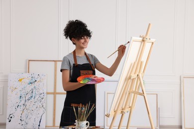 Photo of Young woman painting on easel with canvas in studio