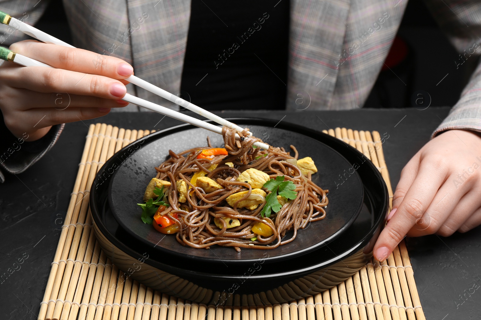 Photo of Stir-fry. Woman eating tasty noodles with meat and vegetables at dark textured table, closeup