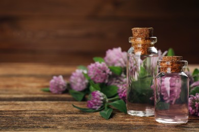 Photo of Beautiful clover flowers and bottles of essential oil on wooden table, closeup. Space for text