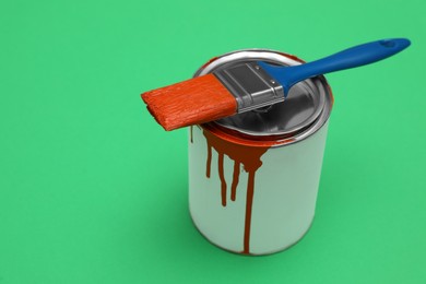 Photo of Can of orange paint and brush on green background. Space for text