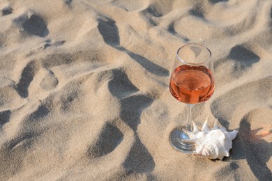 Glass of tasty rose wine and seashell on sand, space for text