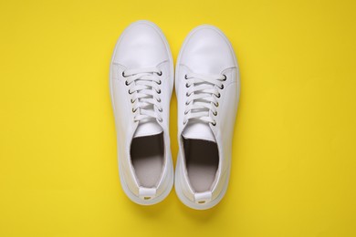 Photo of Pair of stylish white sneakers on yellow background, top view