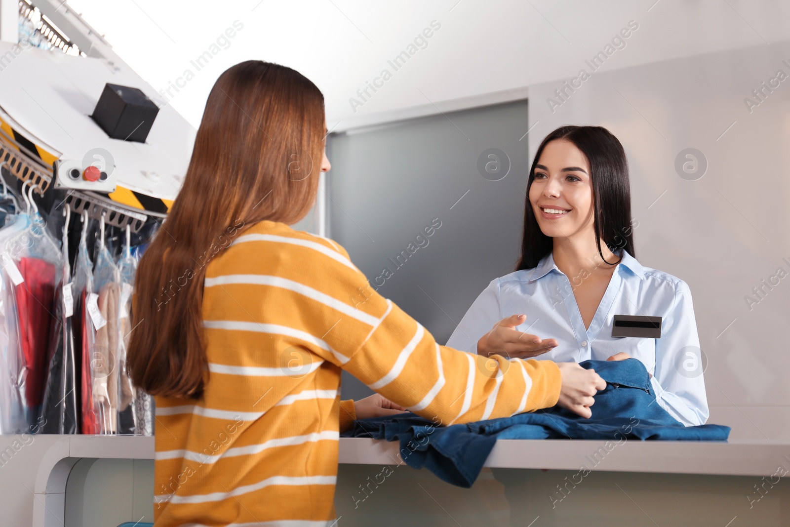 Photo of Female worker receiving clothes from client at modern dry-cleaner's